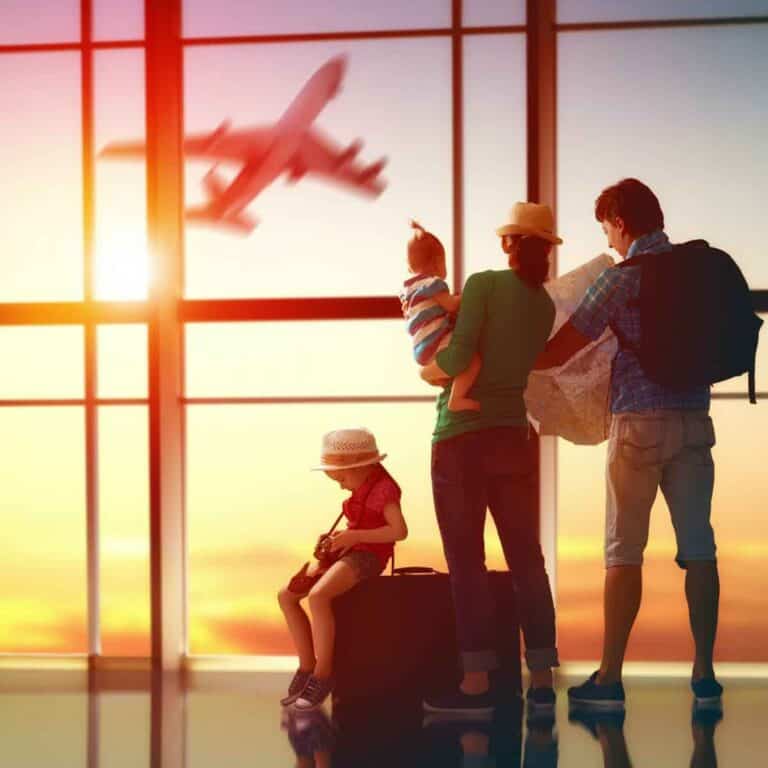 A family standing together inside an airport, watching an airplane take off through large windows.
